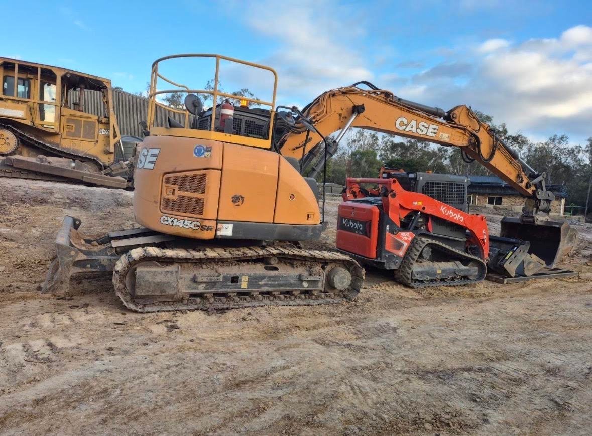 Yellow CASE excavator with red attachment on dirt lot, other construction equipment visible in background