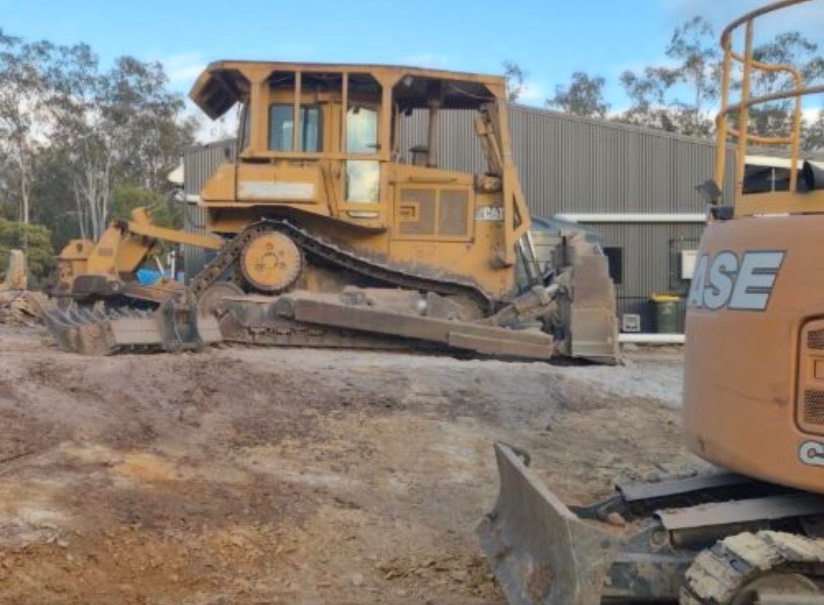 Yellow bulldozer on construction site with other heavy equipment and dirt ground under clear blue sky